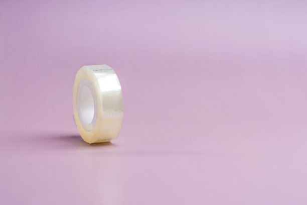 粉红色背景上的一卷窄胶带。站在它的一边图片下载