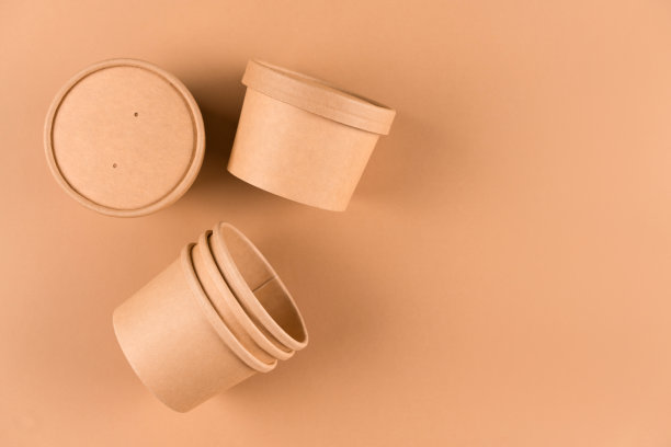 可持续食品包装的概念。棕色一次性牛皮纸汤或冰淇淋容器，杯子与纸帽在浅棕色的背景与拷贝空间，模拟图像图片下载
