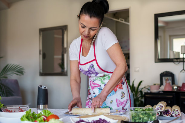 一位年轻的女厨师一边做玉米饼一边用手机打电话。图片下载