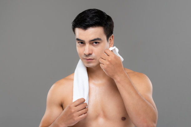 在孤立的灰色工作室背景中，赤裸上身的英俊男子用毛巾擦脸的美容和护肤肖像图片下载