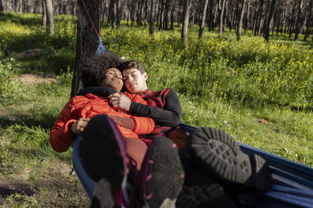 多种族年轻夫妇在森林里的吊床上放松，旅行和休息的概念图片下载