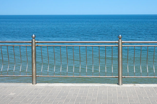 从堤岸眺望大海，有金属栅栏的碎片和铺着瓦片的人行道。极简主义。背景。风景。图片下载
