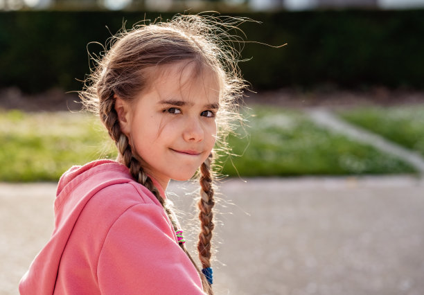 可爱的小女孩的肖像与狡猾的眼神和背光的头发在春天公园看着相机。孩子喜欢在户外玩耍图片下载