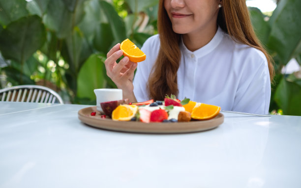 一名年轻女子拿着一块橘子，在餐厅吃混合水果法式吐司早午餐的特写照片图片下载