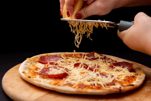 在完成的披萨上用细磨碎器磨碎奶酪图片下载