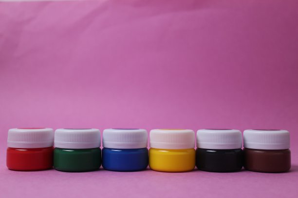 白色盖子的罐子里的颜料排成一排，矗立在粉红色的背景上:丙烯酸、水彩、油画、红、黄、蓝、黑、白，留出文字的空间图片下载