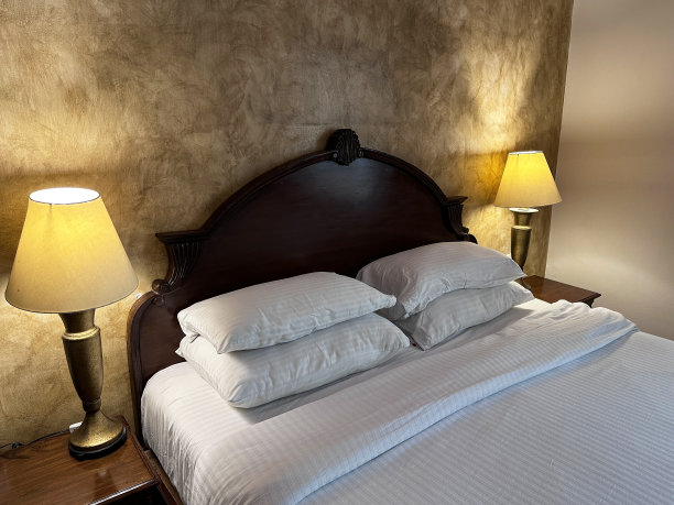 双人床的特写图像，木质床头板，堆叠的白色枕头，白色条纹床罩，床头柜上的电话，照明的电灯，抬高的视野，聚焦于前景图片下载