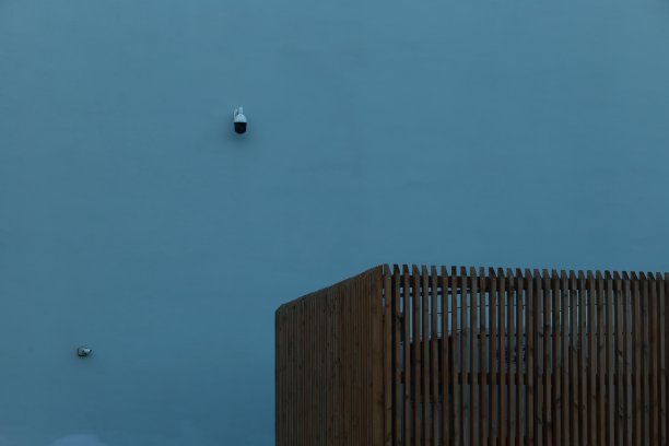 这是一堵装有安全摄像头的蓝色墙，还有一个覆盖着街头垃圾桶的木制屏风。图片下载