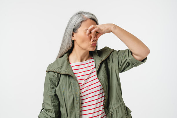 一名中年白人妇女，穿着休闲，头发灰白，散发着恶臭，由于白色背景中散发出的恶臭，她用手捂住了鼻子图片下载