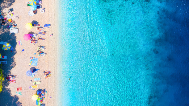 鸟瞰海滩、人群和雨伞。度假和冒险。海滩和蓝色的海水。从无人机上俯瞰海滩和蔚蓝的大海。从无人机上看海岸。图片下载