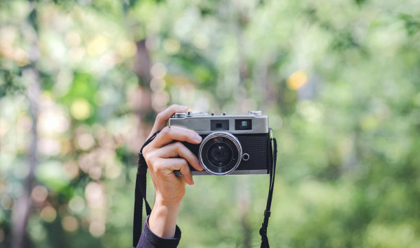 女性手持数码相机绿色自然散景背景图片下载