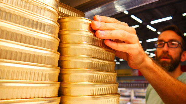 商店货架上许多金罐的特写镜头，一位男顾客拿了一个图片下载