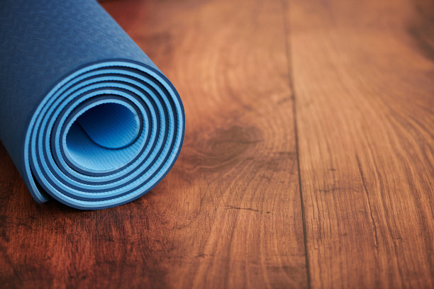 瑜伽课背景与蓝色卷起的瑜伽垫在硬木地板。健康和健康的概念与拷贝空间图片下载