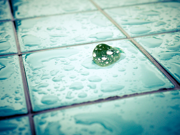 一个小叶子的近距离图像与水滴在湿瓷砖表面。图片下载