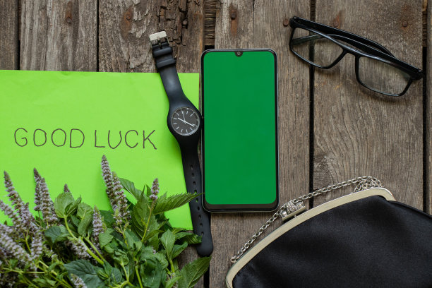 黑色的小包眼镜、手表和手机，绿色的屏幕放在一张旧木桌上，绿色的英文纸上写着“早上好”图片下载