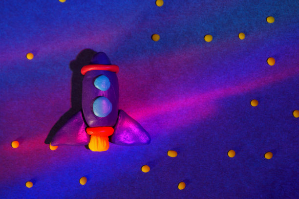 用橡皮泥做成的玩具火箭，背景是蓝色的彩色纸。图片下载