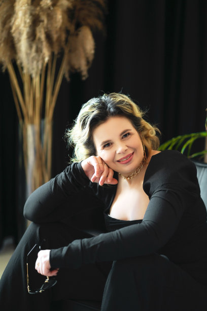 一位身穿黑色西装、面带微笑的女士拿着眼镜坐在那里。图片下载