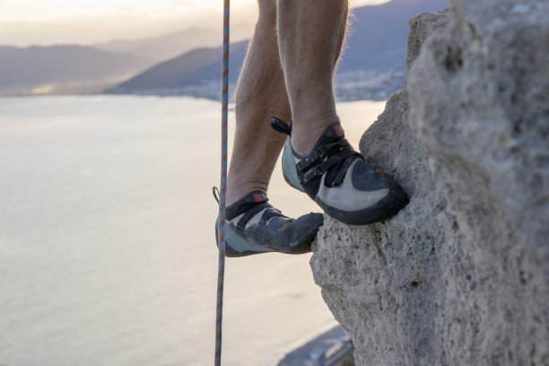 攀爬海上陡峭悬崖的攀岩者的腿图片下载