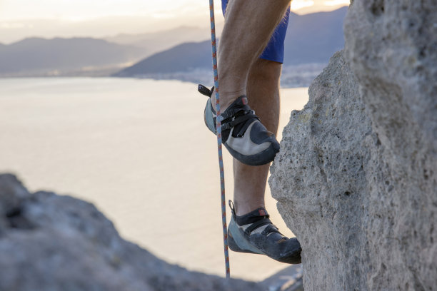 攀爬海上陡峭悬崖的攀岩者的腿图片下载