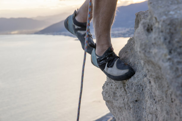 攀岩者的腿攀登海面上陡峭的悬崖图片下载