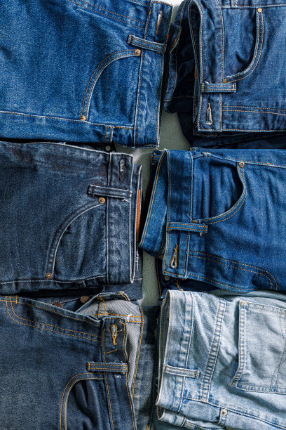 折叠牛仔裤的俯视图，蓝色牛仔裤放在一堆牛仔裤上。白色背景上各种牛仔面料的俯视图。几条长牛仔裤图片下载