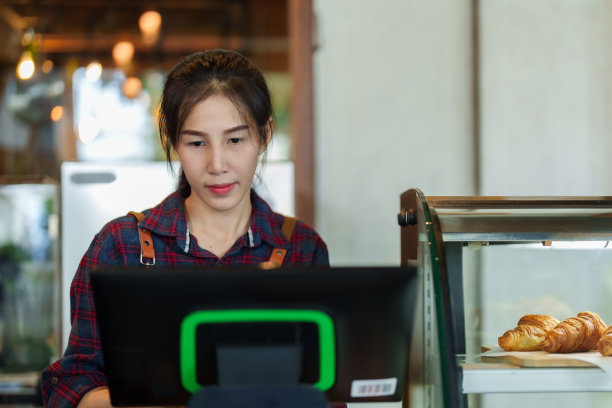 特写:开面包店咖啡馆的亚洲女人，站在机器后面的桌子上，这意味着向顾客收费，店主在店里工作时一直穿着围裙。图片下载