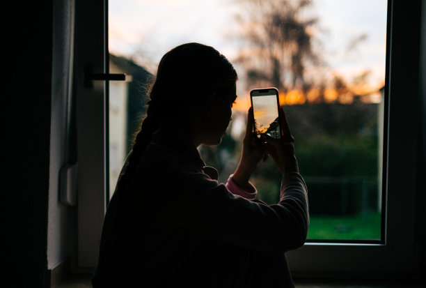 年轻的白人妇女在家里的窗户上拍摄日落。图片下载