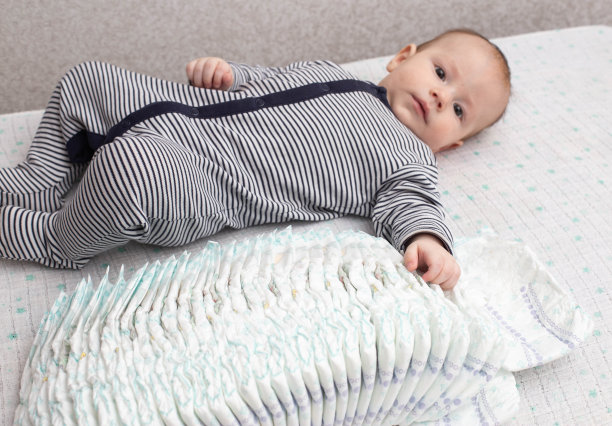 一个穿着条纹西装、蹒跚学步的白人小男孩躺在桌子上，身边放着一叠尿布。文本复制空间图片下载