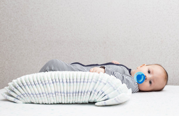 一个穿着条纹西装、蹒跚学步的白人小男孩躺在桌子上，身边放着一叠尿布。文本复制空间图片下载