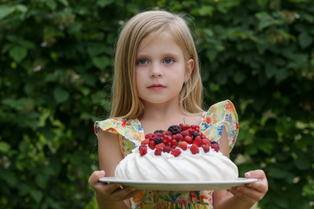 可爱的小女孩的肖像在花夏装拿着托盘与巴甫洛娃蛋糕图片下载