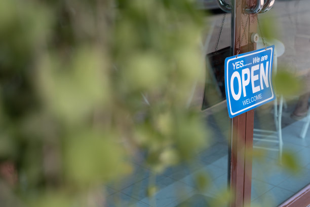 店主在营业的第一天就把招牌从关门改成了开门。保证安全，清洁，戴防护口罩，开咖啡店。向新常态理念开放。图片下载