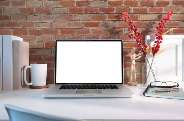 在白色的桌子上用空屏幕、书、相框和杯子模拟笔记本电脑。图片下载