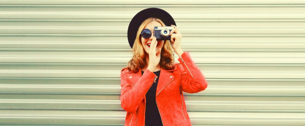 肖像的时尚快乐微笑的女人用胶片相机拍照穿着红色夹克，黑色圆帽的背景图片下载