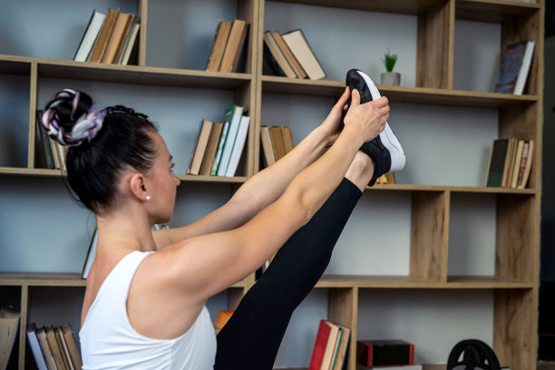 穿着运动服的女子坐在图书馆大厅的垫子上做瑜伽姿势。图片下载