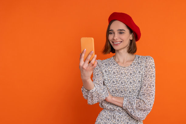 漂亮的成年女子穿着优雅的裙子和红色贝雷帽在手机上自拍。图片下载