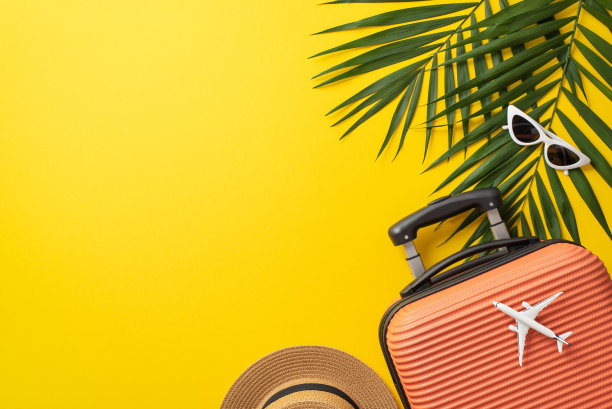 理想的度假概念。橙色手提箱的俯视图照片与棕榈叶，草帽和太阳镜在孤立的亮黄色背景与复制空间图片下载