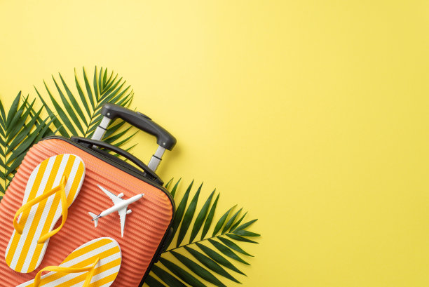 捕捉到度假的气氛。俯视图是一个橙色的行李箱，沙滩配饰，人字拖，黄色背景上的绿色棕榈叶，空白的空间用于文字或促销图片下载