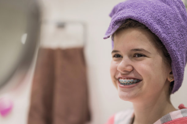 戴着牙套，用毛巾包着湿头发的女孩微笑着，特写图片下载