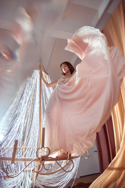 艺术美女在米色粉红色长裙跳舞和旋转大水晶吊灯在大厅中心。幻想时尚女人在一个轻夏季连衣裙图片下载