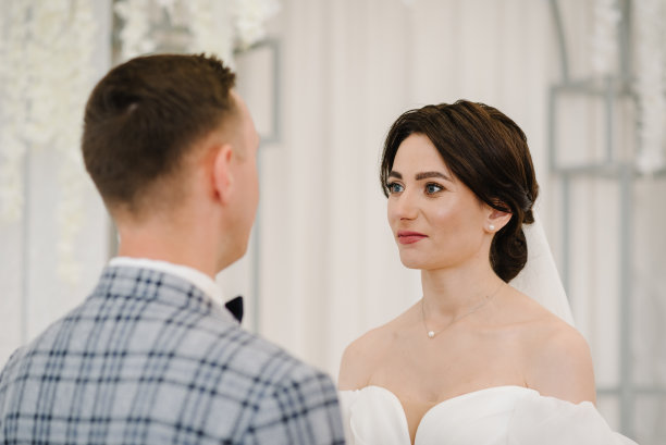 誓言。婚姻。参与。新婚夫妇站在装饰着白花的拱门下举行婚礼。新娘和新郎结婚并戴上结婚戒指。女人和男人同时举行仪式。婚纱照片。图片下载