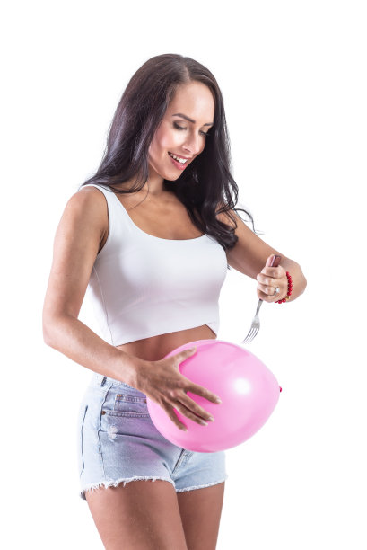 黑发女子拿着一个气球和叉子刺气球，以显示疼痛缓解胃膨胀和抽筋。孤立的背景。图片下载
