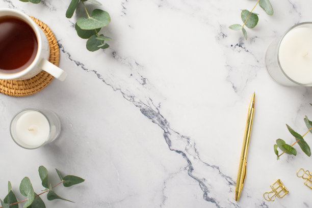 经营理念。俯视图照片的蜡烛杯茶在藤服务垫金笔活页夹和桉树在白色大理石的背景与copyspace图片下载