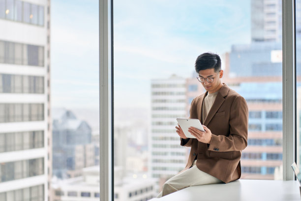 年轻的亚洲商人、高管坐在现代办公室里使用平板电脑。图片下载