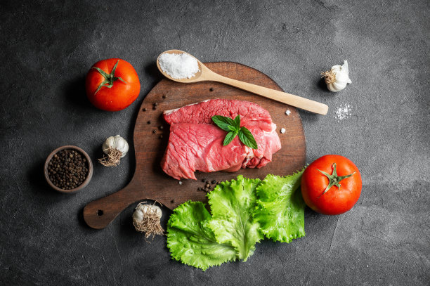 生牛肉牛排肉砧板上质朴的背景与薄荷叶，辣椒和生菜，屠夫的概念图片下载