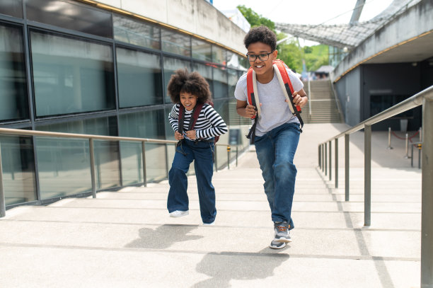 学生们背着书包，穿着休闲衬衫和牛仔裤，在楼梯上奔跑。图片下载