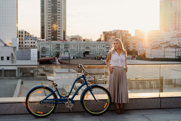 活跃时尚的金发女人与一辆复古自行车在城市的背景在日落。图片下载