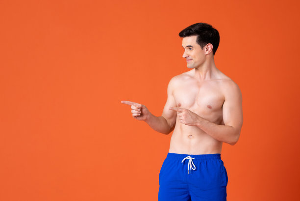 微笑的英俊男子赤膊指着手指复制空间旁边的橙色工作室背景图片下载