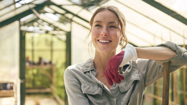在家里的温室里拿着扫帚工作的微笑妇女的肖像图片下载