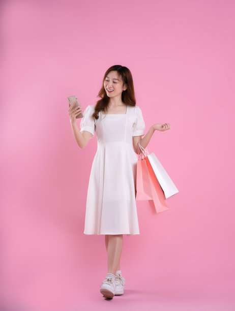 亚洲女性拿着购物袋，在粉色背景上摆姿势的全身照片图片下载