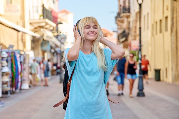 年轻女子戴着耳机背着背包在旅游城市的街道上图片下载